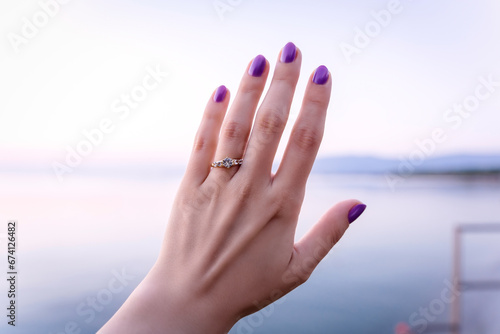 Woman's hand with a proposal diamond ring by the sea, sunrise on beach proposal, white sapphire golden ring photo