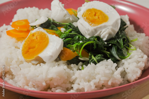 a menu of white rice with clear vegetables of spinach leaves and carrots and a salted egg on a wooden board isolated on a white background
