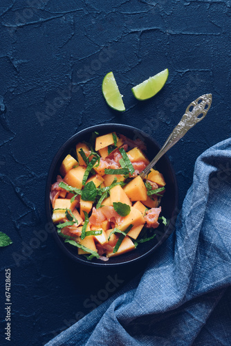 Healthy salad with salmon, melon, mint and lime in a black bowl
