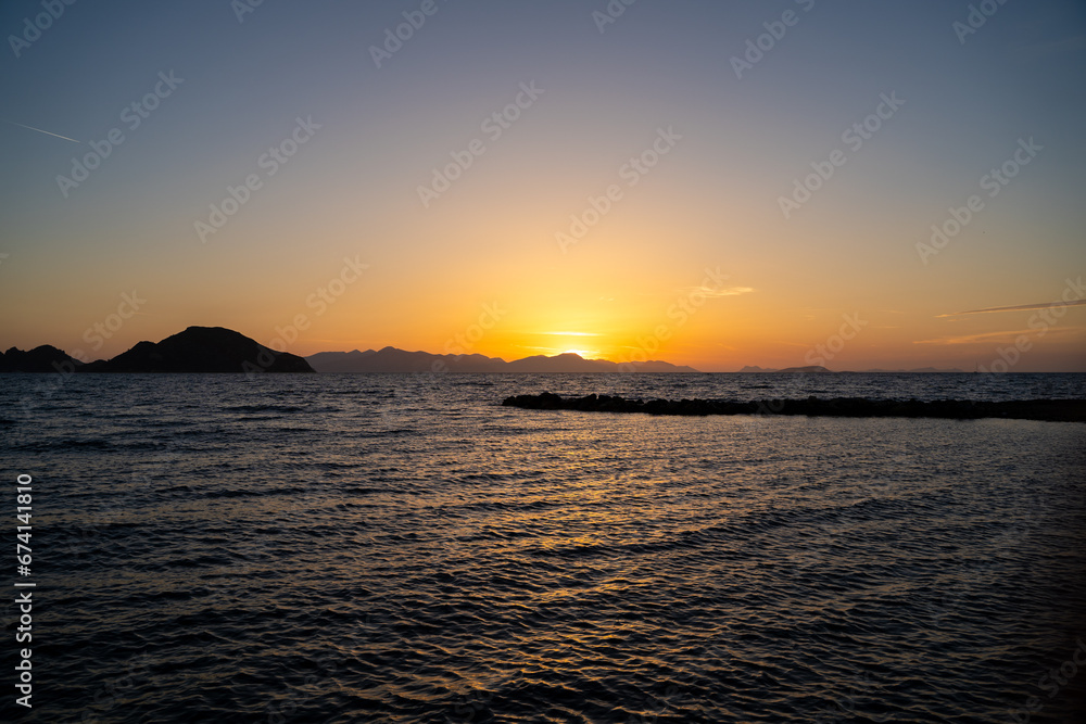 View of sea and island silhouette at sunset golden hour.