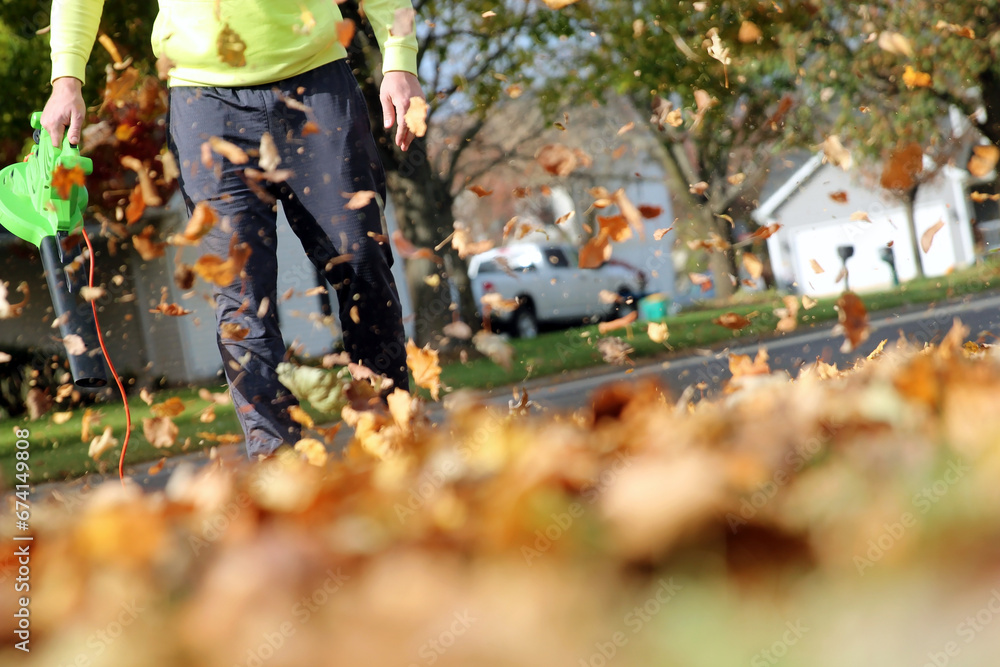 Man working with leaf blower: the leaves are being swirled up and down on a sunny day Man working with leaf blower: the leaves are being swirled up and down on a sunny day