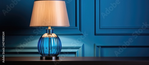 A trendy color scheme for your interior includes a blue lampshade and a table lamp with a glass element near a light wall all complemented by a grey cloth photo