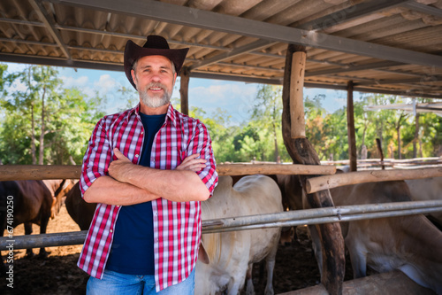 Portrait of happy senior man cattle farmer owner wearing a cowboy hat standing arms crossed and looking at camera on a countryside farm.
