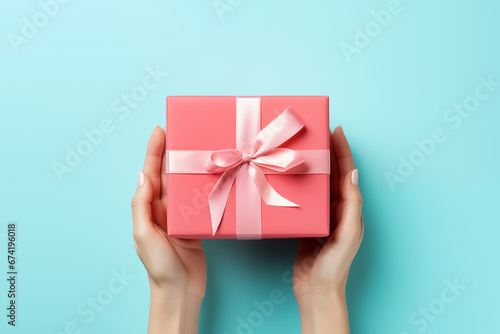 Photo of female hands holding a gift with a ribbon on blue background. Concept of holidays and gifts. AI generated content. © Andrii