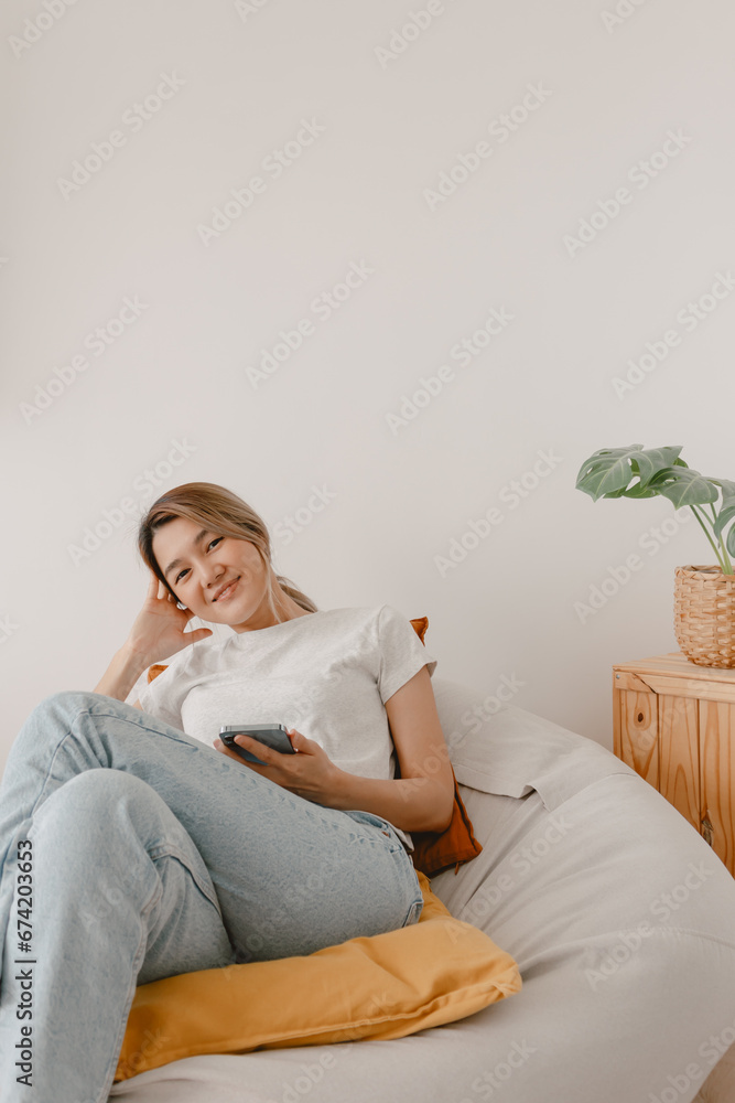Asian woman sitting on beanbag and using smartphone. Asian woman sitting on beanbag and using smartphone.