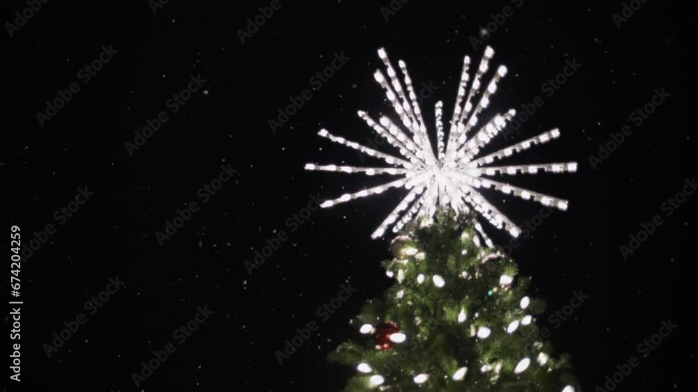 Illuminated star decoration on top of a Christmas tree with falling snow at night. Slow motion. Illuminated star decoration on top of a Christmas tree with falling snow at night. Slow motion.