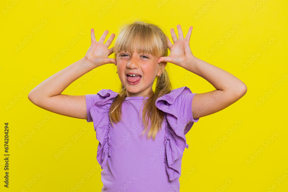 Cheerful funny bully young cute girl showing tongue making faces at camera, fooling around, joking, aping with silly face, teasing. Preteen blonde child kid on yellow background. Little children Cheerful funny bully young cute girl showing tongue making faces at camera, fooling around, joking, aping with silly face, teasing. Preteen blonde child kid on yellow background. Little children