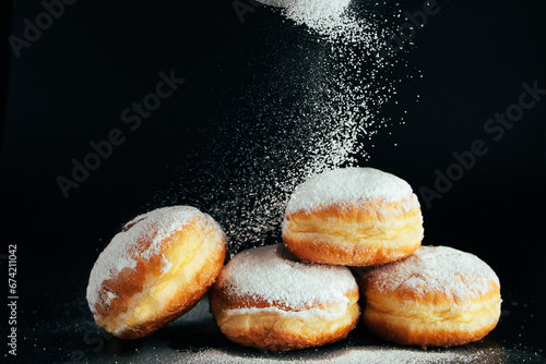Powdered sugar is poured onto donuts. Traditional Jewish dessert Sufganiyot on black background. Cooking fried Berliners. © Galina Atroshchenko