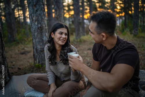Young couple man and woman boyfriend and girlfriend or husband and wife in love relationship hold paper cup of coffee or tea while spend time together in the park forest bonding love real people © Miljan Živković