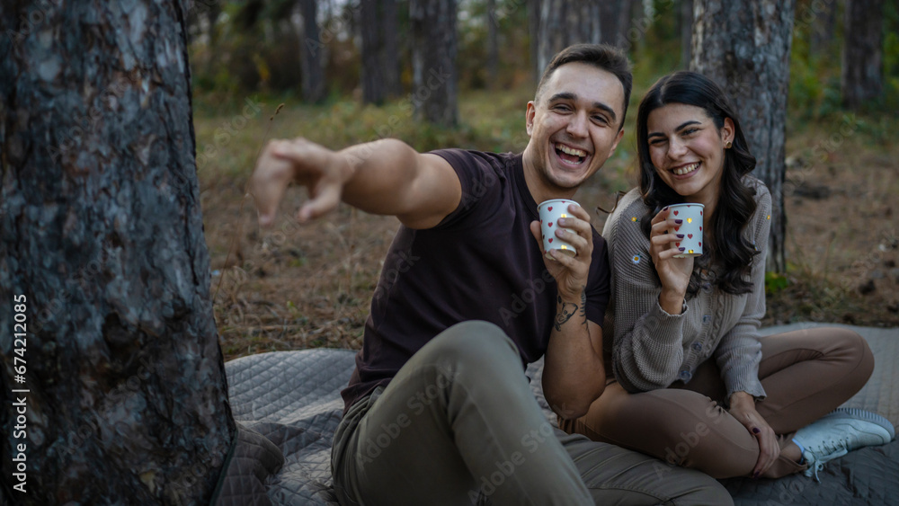 Young couple man and woman boyfriend and girlfriend or husband and wife in love relationship hold paper cup of coffee or tea while spend time together in the park forest bonding love real people