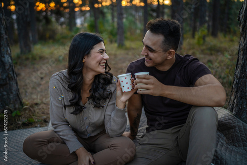 Young couple man and woman boyfriend and girlfriend or husband and wife in love relationship hold paper cup of coffee or tea while spend time together in the park forest bonding love real people