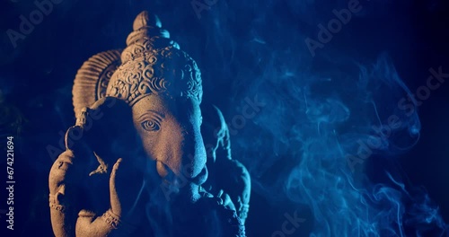 Ganesha idol made of sandstone on a black background at night. There is warm light and blue light. There is smoke from the incense that people burn to worship. photo