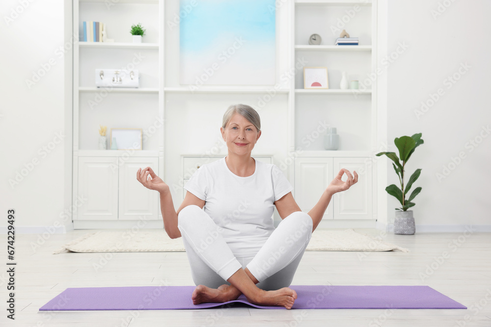 Happy senior woman practicing yoga on mat at home Happy senior woman practicing yoga on mat at home