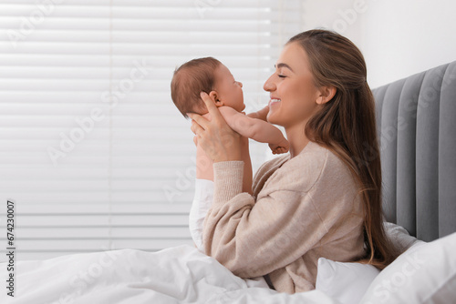 Mother holding her cute newborn baby in bed indoors, space for text