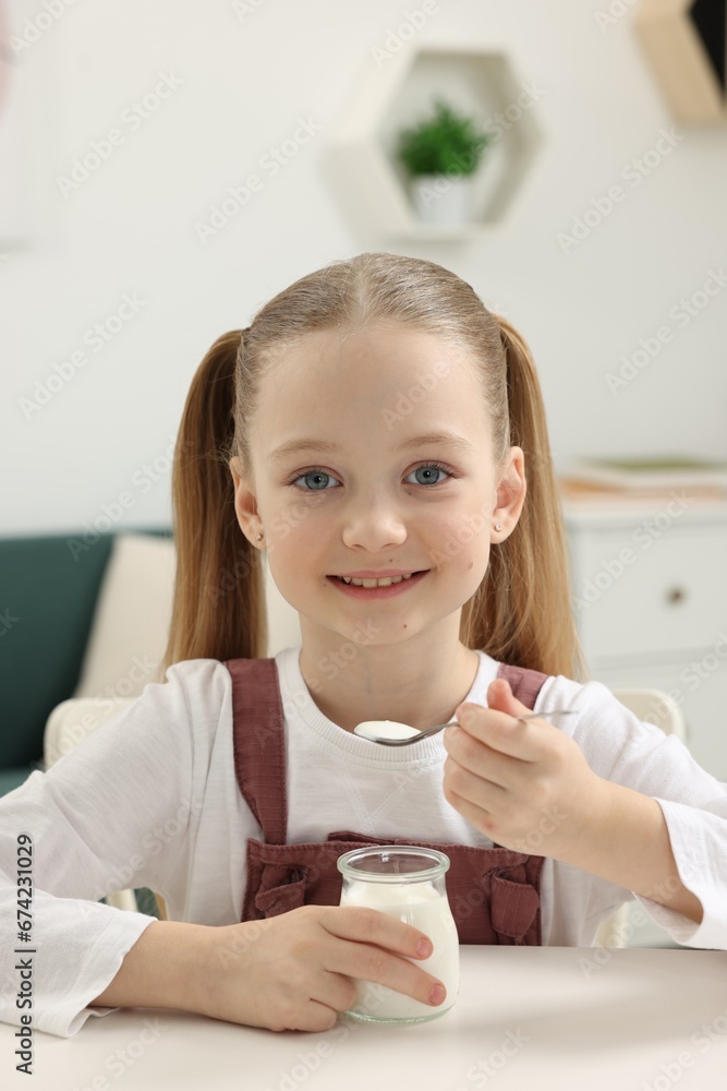 Cute little girl with tasty yogurt at white table indoors Cute little girl with tasty yogurt at white table indoors