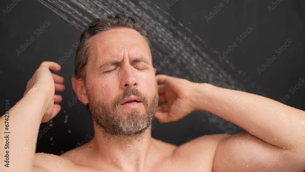 Muscular man washing hair in bath. Guy bathing shower head in bathtub