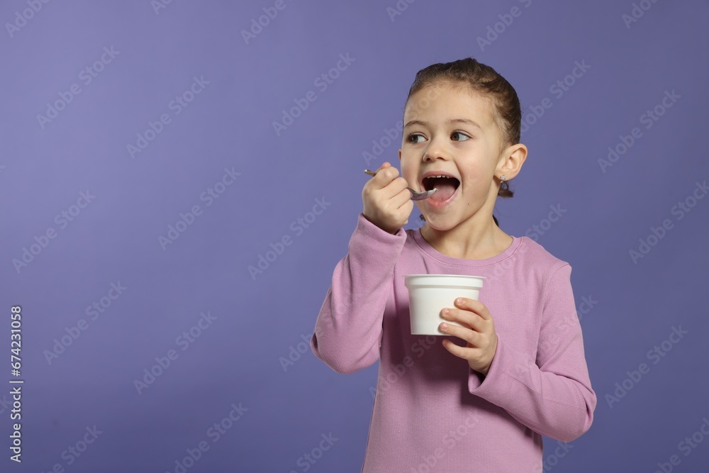 Girl eating tasty yogurt on violet background, space for text Girl eating tasty yogurt on violet background, space for text