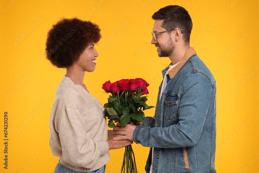 International dating. Handsome man presenting roses to his beloved woman on orange background International dating. Handsome man presenting roses to his beloved woman on orange background