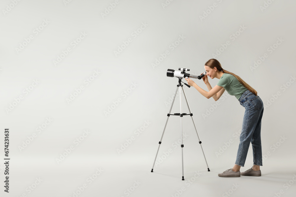 Young astronomer looking at stars through telescope on grey background, space for text