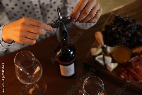 Romantic dinner. Woman opening wine bottle with corkscrew at table indoors, above view