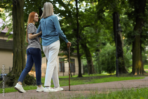 Senior lady with walking cane and young woman in park, back view. Space for text