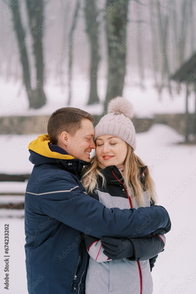 Smiling boyfriend and girlfriend hugging while standing in a snowy park