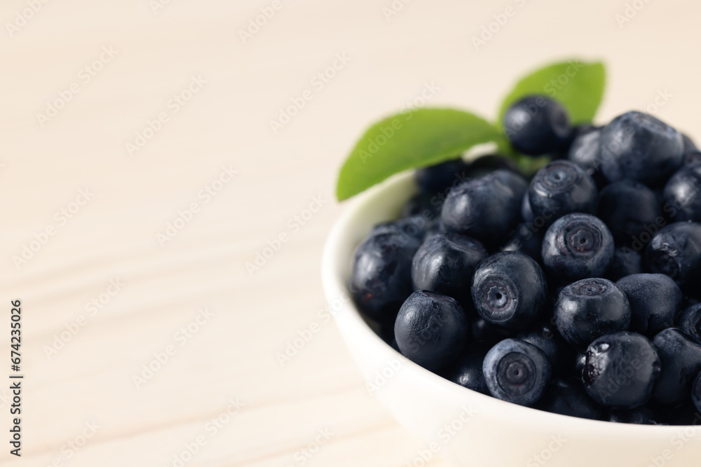 Tasty fresh bilberries with leaves in bowl on white table, closeup. Space for text Tasty fresh bilberries with leaves in bowl on white table, closeup. Space for text