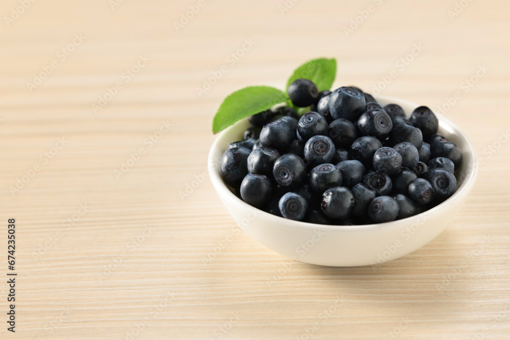 Tasty fresh bilberries with leaves in bowl on light table. Space for text Tasty fresh bilberries with leaves in bowl on light table. Space for text