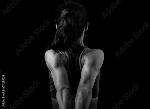 Strong sporty woman doing the arms and shoulders stretching exercise holding the hands in fist behind the back to relaxing back side of body in sport wear. Closeup