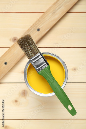 Can of yellow paint with brush on wooden table, top view