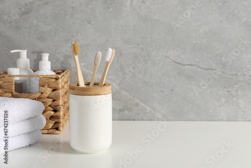 Bamboo toothbrushes in holder, towels and cosmetic products on white countertop, space for text