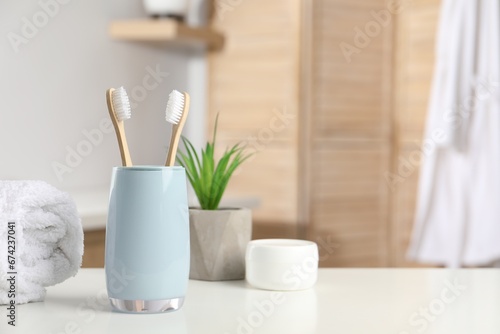 Bamboo toothbrushes, towel, potted plant and cosmetic product on white countertop in bathroom, space for text