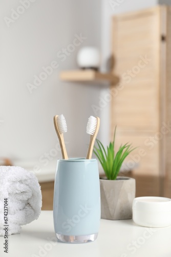 Bamboo toothbrushes, towel, potted plant and cosmetic product on white countertop in bathroom