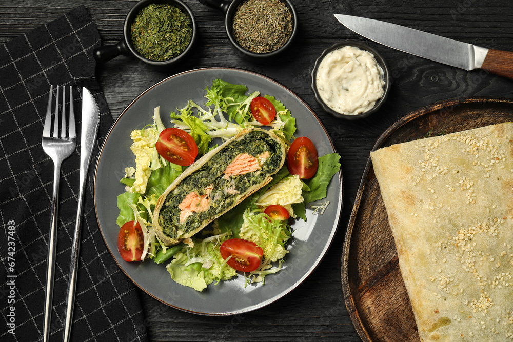 Piece of tasty strudel with salmon, spinach and salad on black wooden table, flat lay Piece of tasty strudel with salmon, spinach and salad on black wooden table, flat lay
