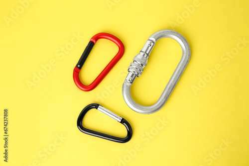 Metal carabiners on yellow background, flat lay
