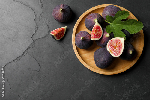 Plate with fresh ripe figs and green leaf on black table, flat lay. Space for text