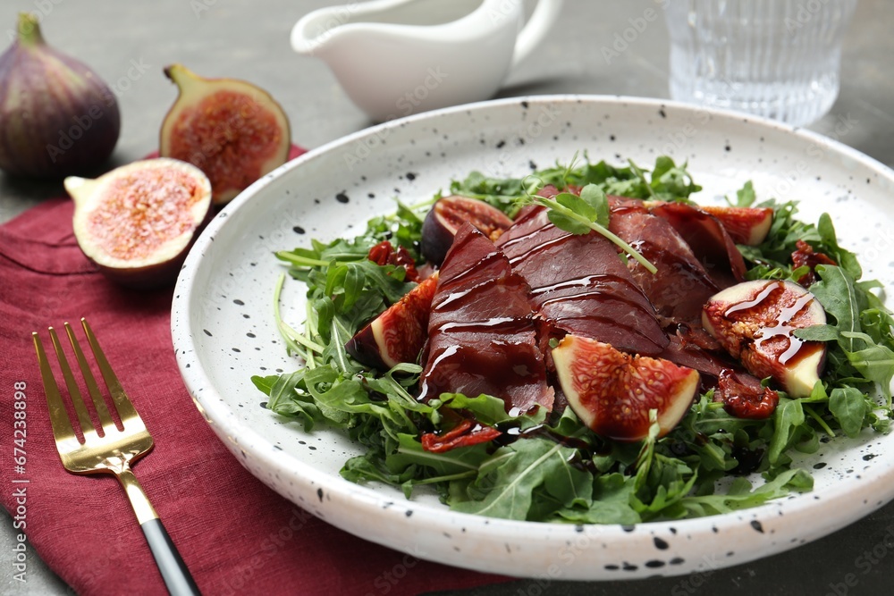 Plate of tasty bresaola salad with figs, sun-dried tomatoes, balsamic vinegar and fork on table, closeup