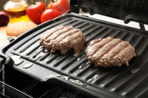 Delicious hamburger patties cooking on electric grill, closeup