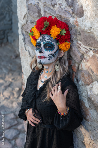 Young woman with painted skull on her face for Mexico's Day of the Dead (El Dia de Muertos) against color background