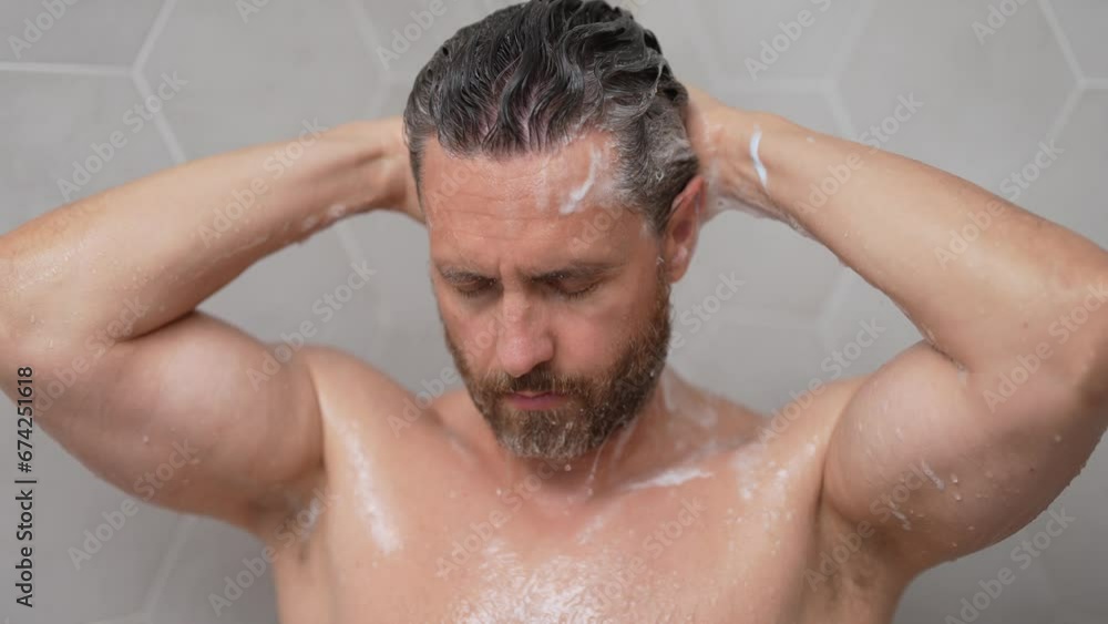 Middle aged man washing hair in bath. Guy bathing shower head in