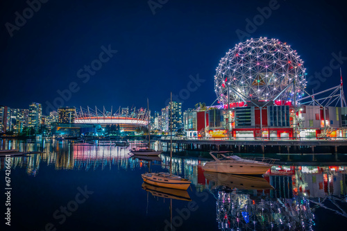 Skyline of downtown Vancouver, BC Place Stadium and Science World museum at night with light reflecting on water, boats in False Creek, British Columbia, Canada. Photo taken in October 2021.