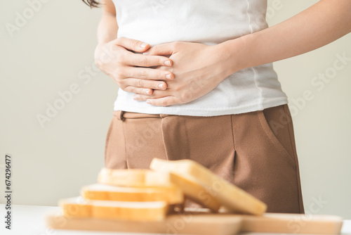 Gluten allergy, asian young woman hand push out, refusing to eat white bread slice on chopping board in food meal at home, girl having a stomach ache. Gluten intolerant and Gluten free diet concept. photo