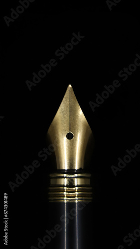 closeup macro shot of the gold tip of a luxury fountain ink pen used for calligraphy isolated in a black background