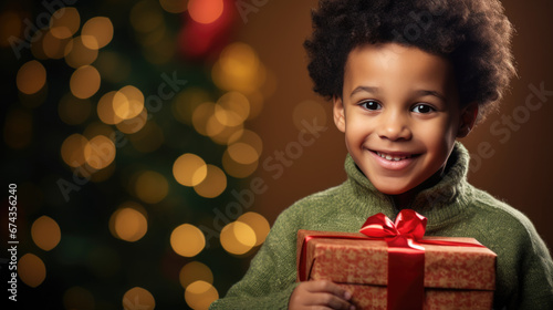 A delighted boy with a beaming smile holds a Christmas present , surrounded by the festive glow of tree lights and ornaments. © MP Studio