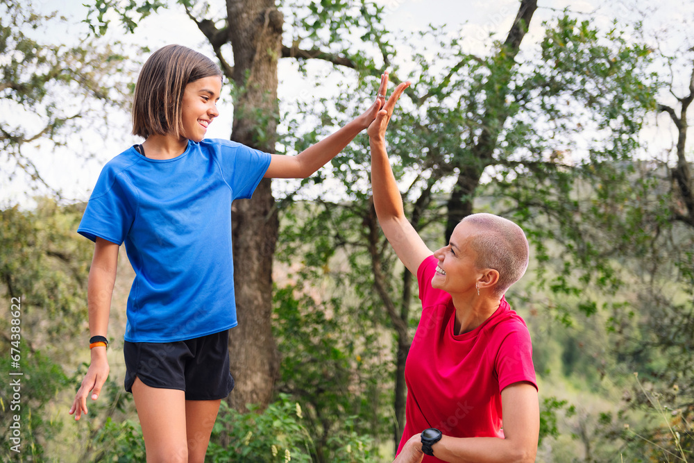 Fototapeta premium mother and daughter giving a high five during their training in the woods, concept of sport with children in nature and active lifestyle
