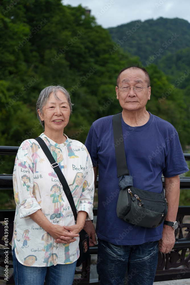 老夫婦が旅先の山を背景に撮った記念写真