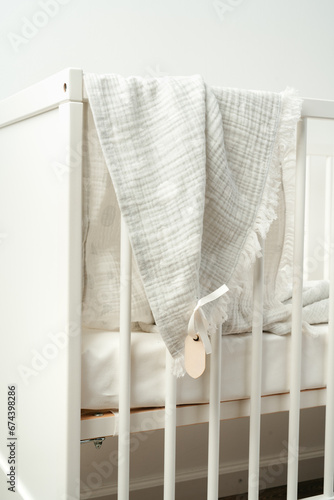 Cotton baby blanket with paper tag hanging from baby bed © fotofabrika