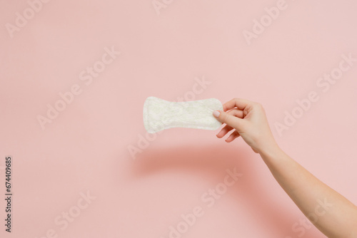 Sanitary napkin in woman's hand on pink background