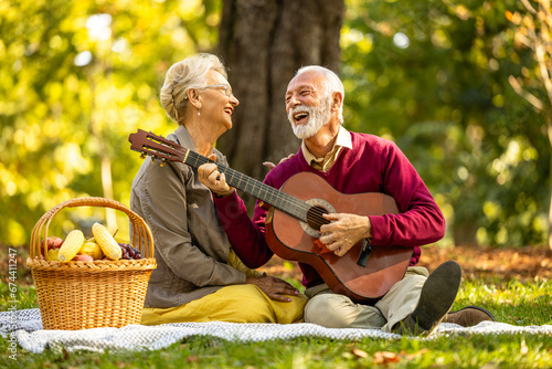 Elderly couple in love on picnic enjoying autumn and relaxing with guitar. © littlewolf1989