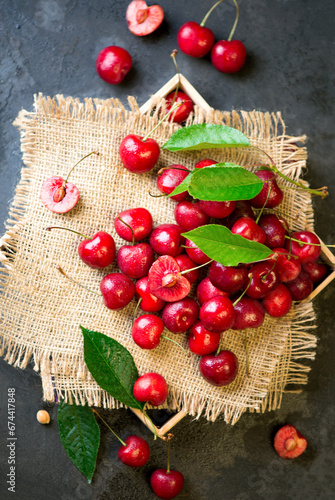Sweet red cherry on burlap on a black background. A large number of cherries with leaves on the table, on a black background. close-up.